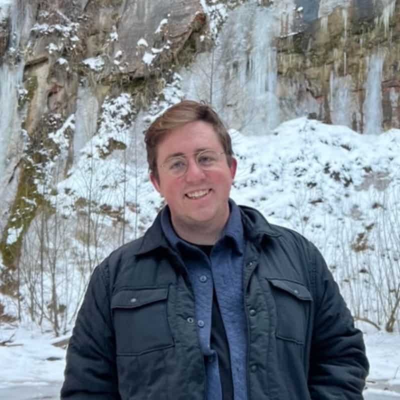 A person smiling for the camera with a snowy, icicle-adorned cliff in the background.