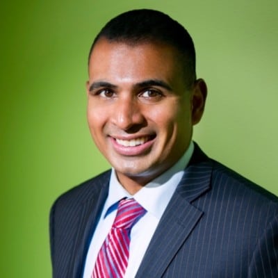 Professional man smiling confidently in a suit with a green background.