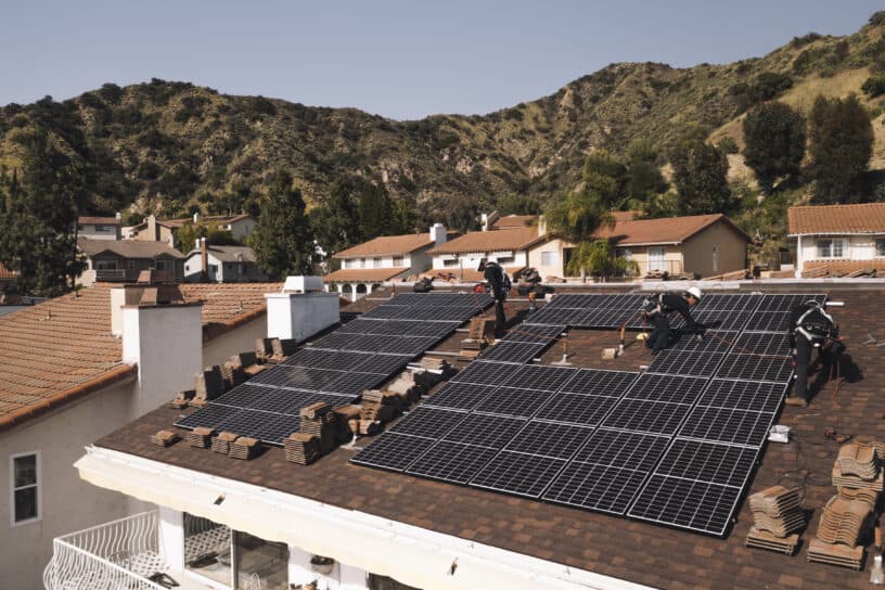 A neighborhood with houses equipped with solar panels on their roofs, showcasing residential renewable energy adoption against a backdrop of hills