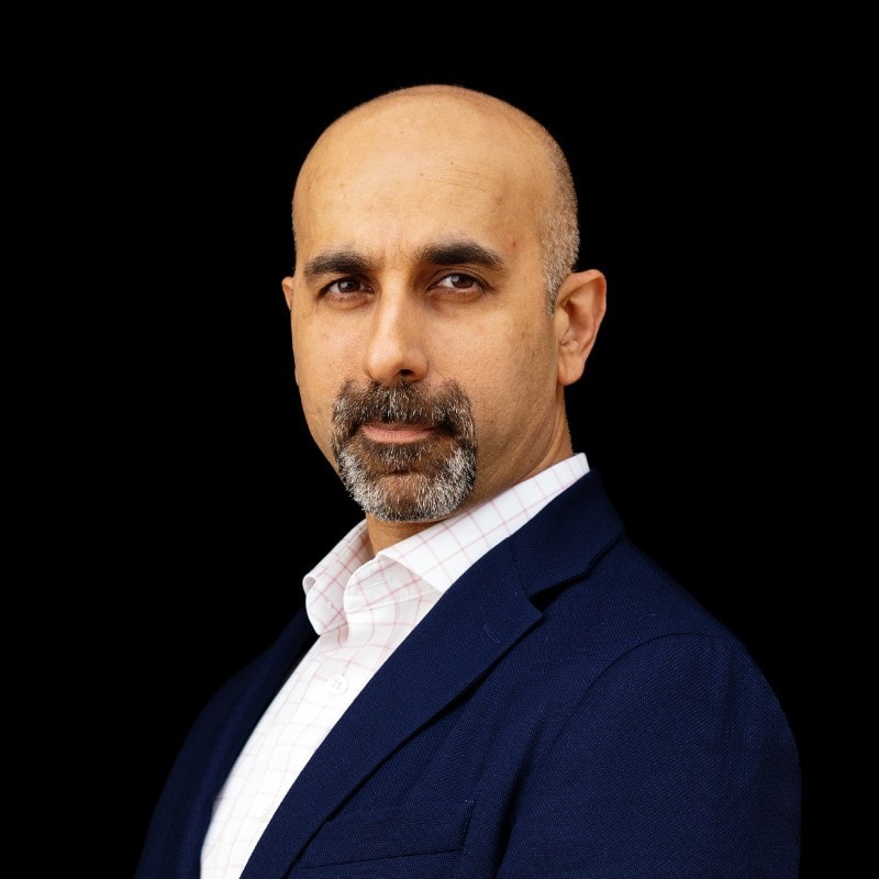 Portrait of a confident man with a beard in professional attire against a black background.