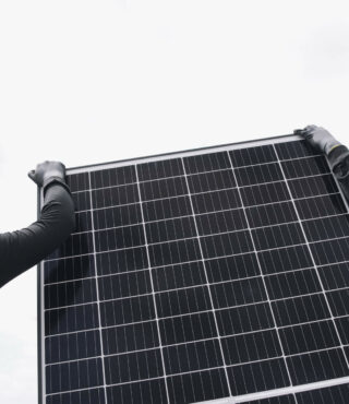 Workers in hard hats and safety gear installing a solar panel under a cloudy sky.