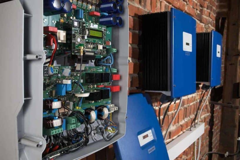 An open industrial electrical panel revealing intricate electronic components mounted on a brick wall accompanied by two closed blue electrical boxes