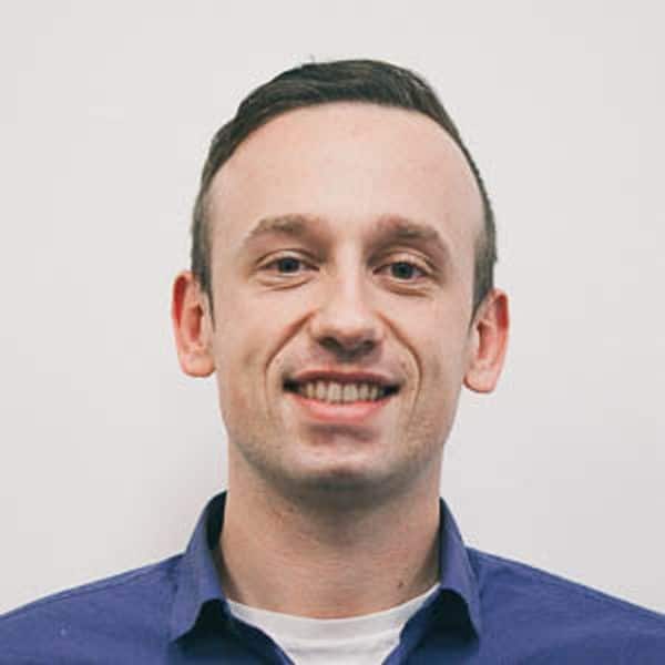 A smiling man with a clean-shaven face, featuring short, neatly-styled hair, against a plain white background. he is wearing a dark blue shirt.