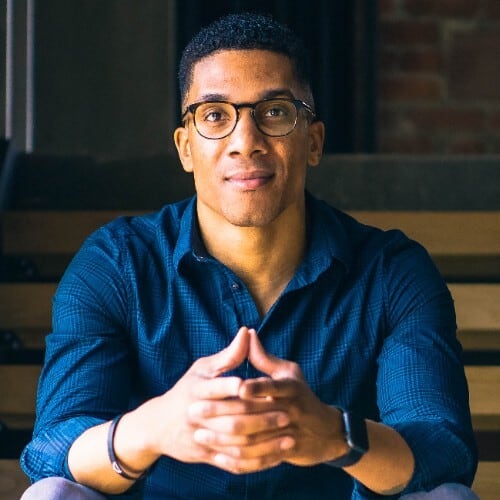 Confident young professional with a friendly demeanor sitting casually with interlocked hands, poised for an engaging conversation.