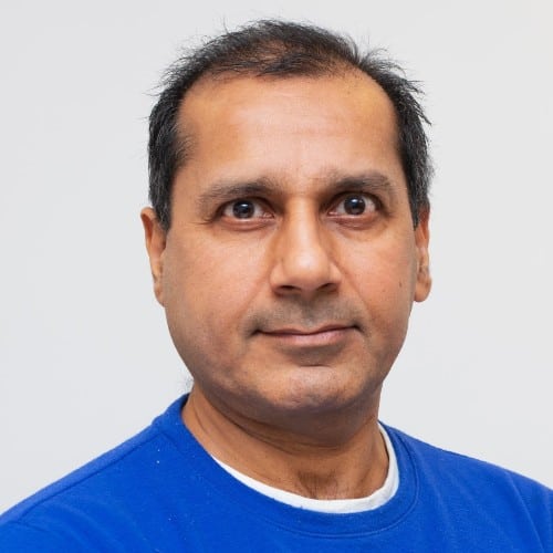 Portrait of a man with a neutral expression, wearing a blue shirt against a grey background.