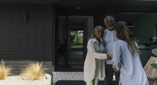 A warm welcome at the front door as a smiling couple greets a visitor.