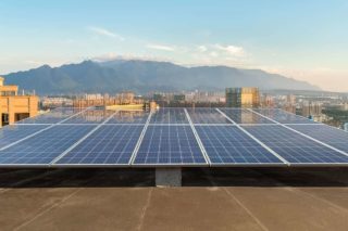 Rooftop lined with solar panels against an urban and mountain backdrop