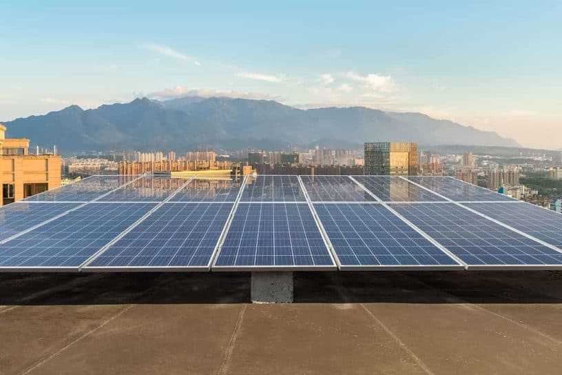 Rooftop lined with solar panels against an urban and mountain backdrop