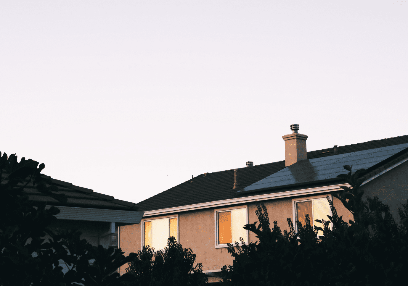 A tranquil suburban evening with the warm glow of sunset reflecting off the side of a house.