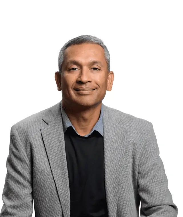 Confident professional man with a gentle smile, dressed in a smart grey blazer over a black shirt, posing against a white background.