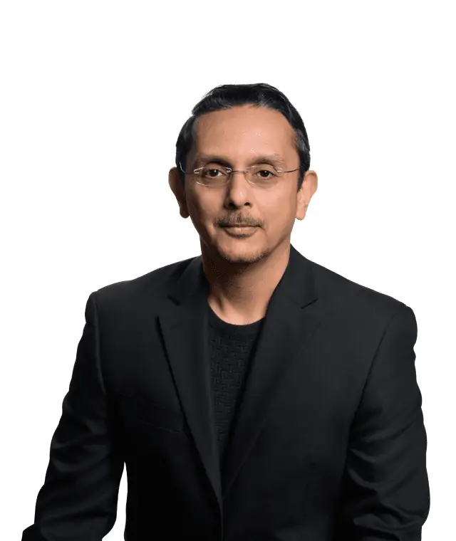 A man in a black blazer with a serious expression, standing against a white background.