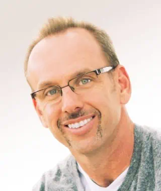 A smiling man with glasses against a light background.