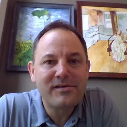 A smiling person posing for a selfie with colorful artwork on the wall in the background.