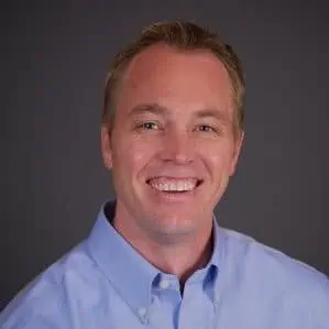 Smiling man in a blue shirt against a grey background.